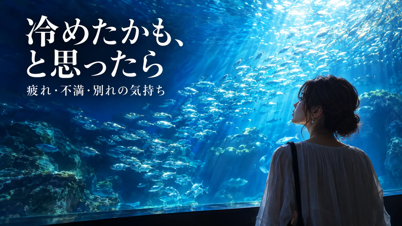 青い水槽の魚の群れを眺めながら気持ちを整理する女性